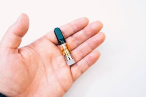 A man's hand holds a vape cartridge. It contains THC.