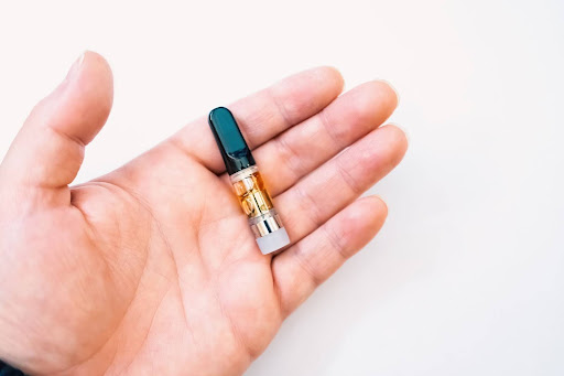 A man's hand holds a vape cartridge. It contains THC.